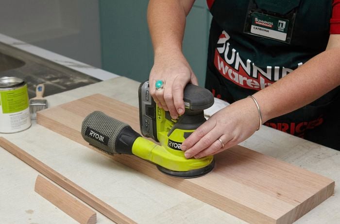 Person using orbital sander on wooden shelf.
