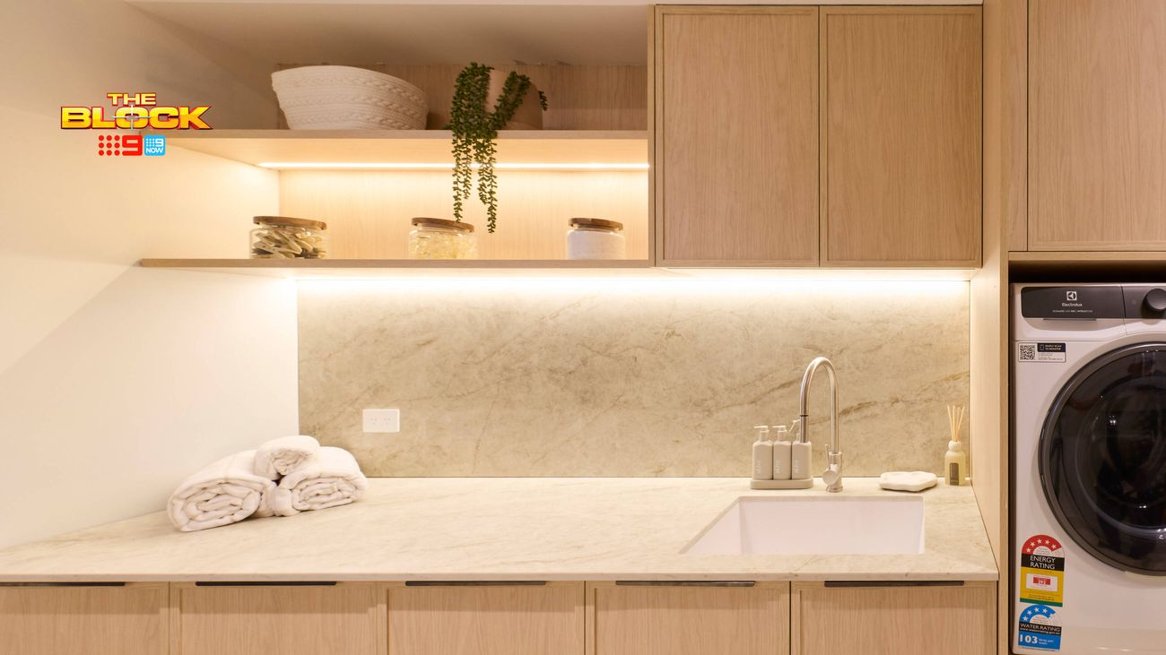 Modern laundry featuring light timber cabinetry, stone benchtop and splashback, open shelving, sink and integrated washing machine.