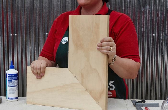 An assembled corner shelf, yet to be painted, held by a Bunnings team member