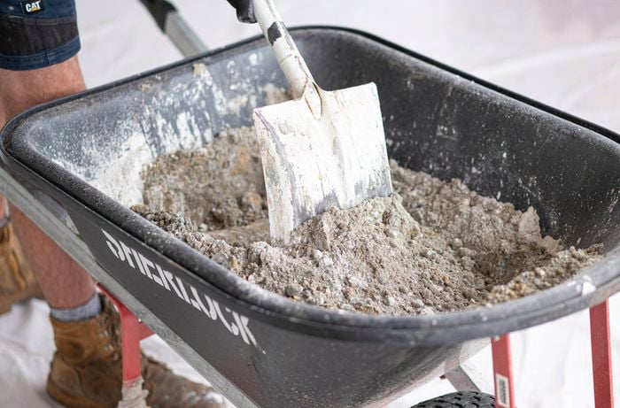 A person is mixing dry mortar mix ingredients in a wheelbarrow using a shovel
