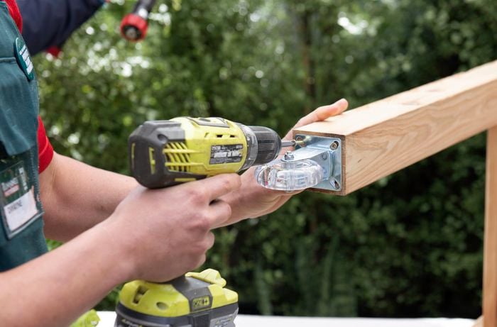 A person attaching a castor wheel to the end of a piece of timber using a cordless drill