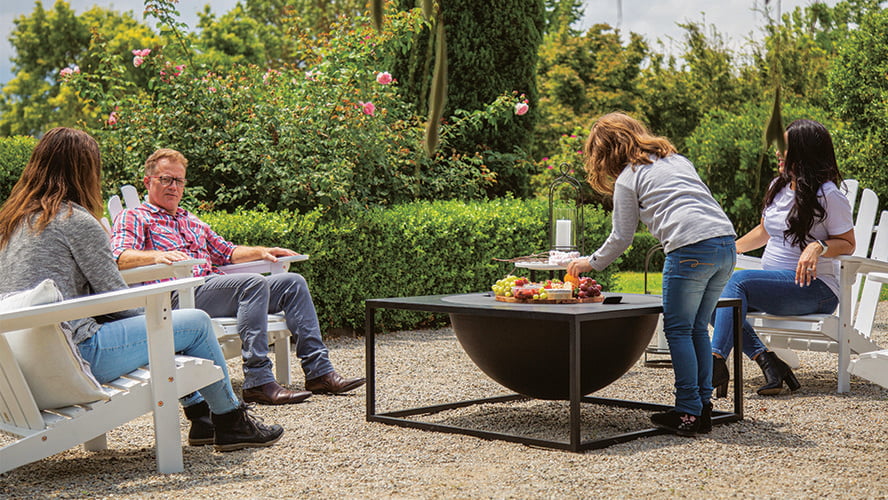 Four people in deckchairs in an outdoor setting, a platter of food on a closed firepit between them