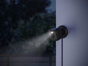 A black security camera with a light on it attached to an outside wall.