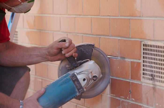An angle grinder being used to cut vertical lines into a brick wall