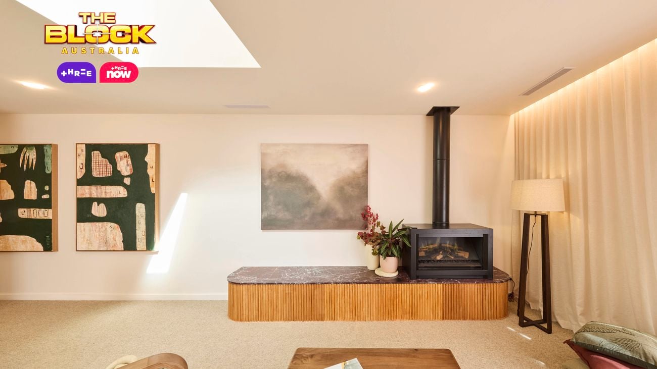 A modern living room with a skylight, featuring a fireplace, wall-mounted artwork, and a variety of contemporary furniture pieces.