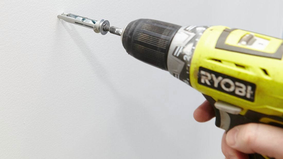 Close-up of a cordless driver screwing in a metal wall anchor screw