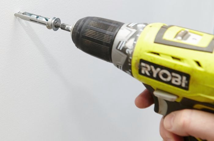 Close-up of a cordless driver screwing in a metal wall anchor screw