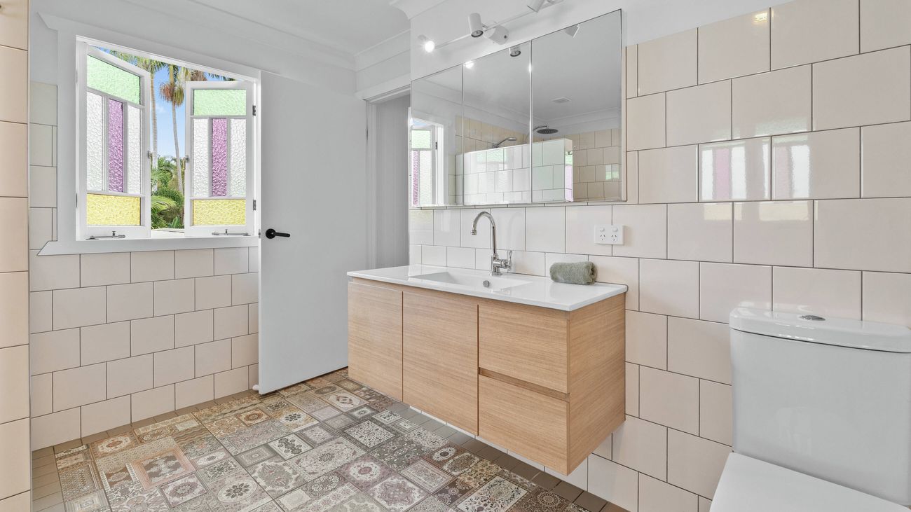 Bathroom with a wooden vanity, white subway tiles, patterned floor tiles and a window with coloured glass
