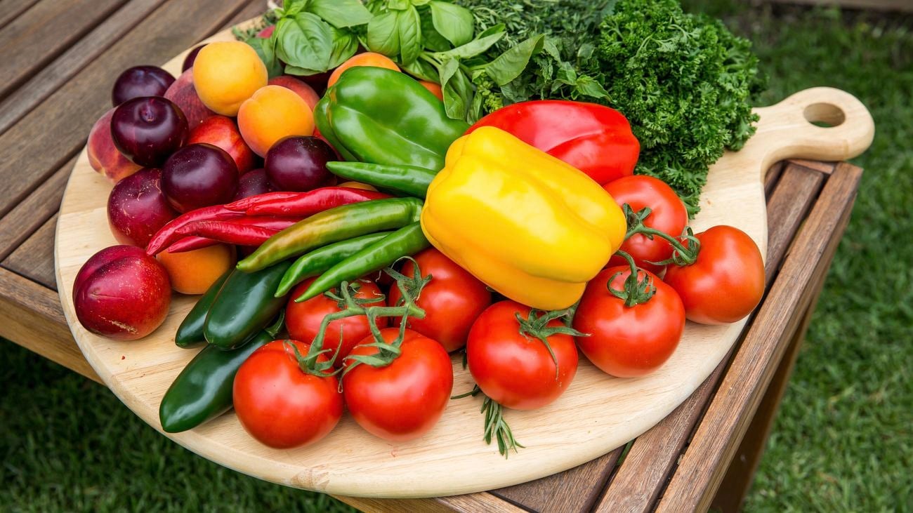 Capsicums, tomato, chili and plums laid out on a table