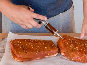 Person injecting meat with a marinade injector