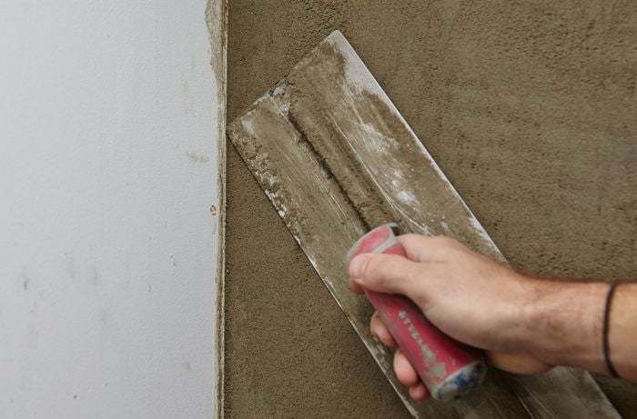 A person running a trowel towards the corner of a plastered wall