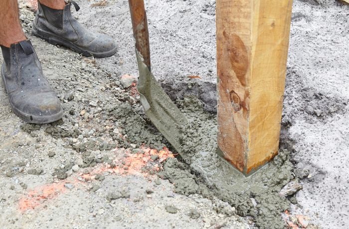 A posthole with a post positioned in it being filled with concrete