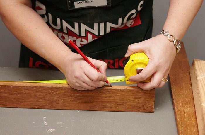 Person using measuring tape to measure side of pine frame.
