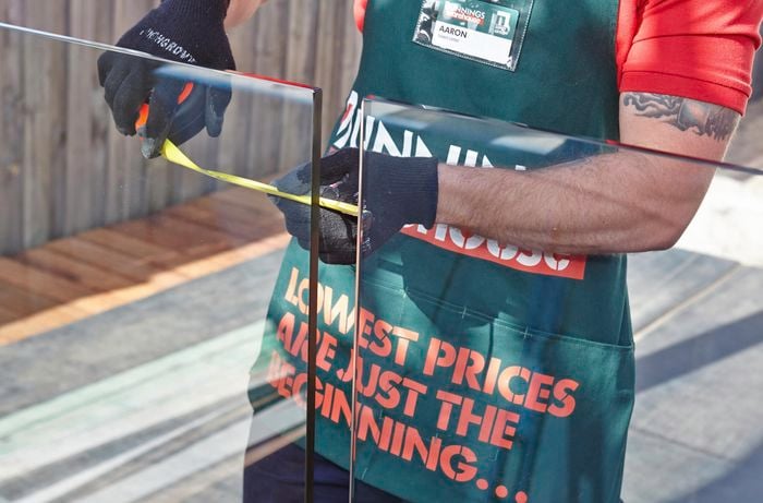 Person measuring gap between glass fence panels.