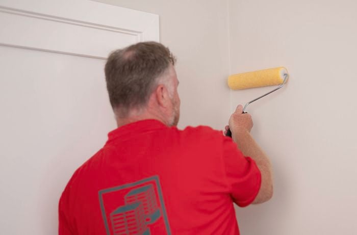 A Bunnings team member is using a paint roller to apply wallpaper adhesive