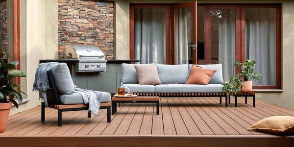 A Barbecue and outdoor setting on a timber decking with a cushion and pot plants on it.