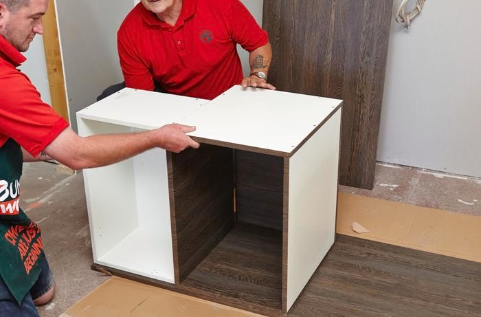 Two people positioning two cabinet units on a side panel