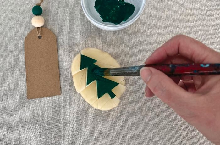 Hand paints green Christmas tree onto carved side of potato