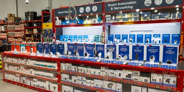Wide view of a smart home security display in a Bunnings store, featuring shelves stocked with Ring, Eufy, Arlo, Swann, Blink and Orion security cameras, video doorbells and surveillance systems. Overhead signage reads “Smart Security” and “Smart Automation & Networking.”