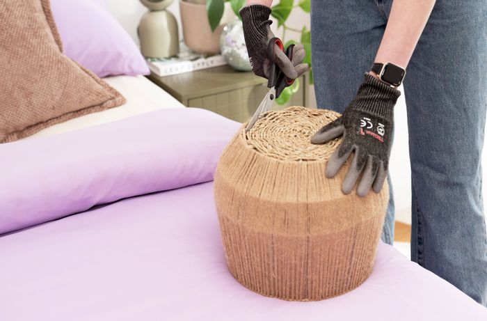 A person is carefully cutting the base of a woven basket to create an opening for a DIY pendant light shade