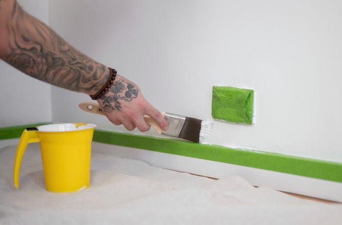 A person adorned with a hand tattoo and wearing a beaded bracelet is applying paint to the walls with a paint brush.