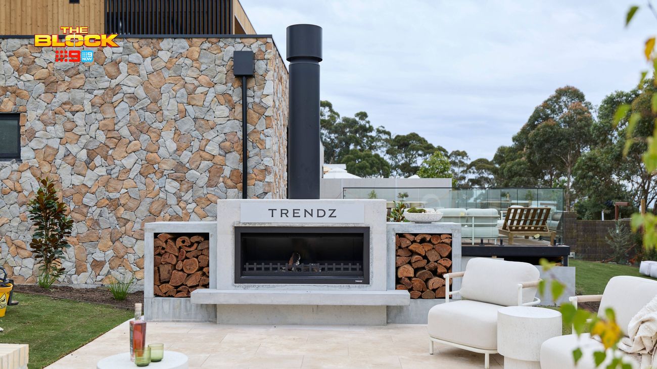 Modern outdoor entertaining area featuring a built-in fireplace with stacked firewood, stone feature wall, white lounge seating and glass balustrade.