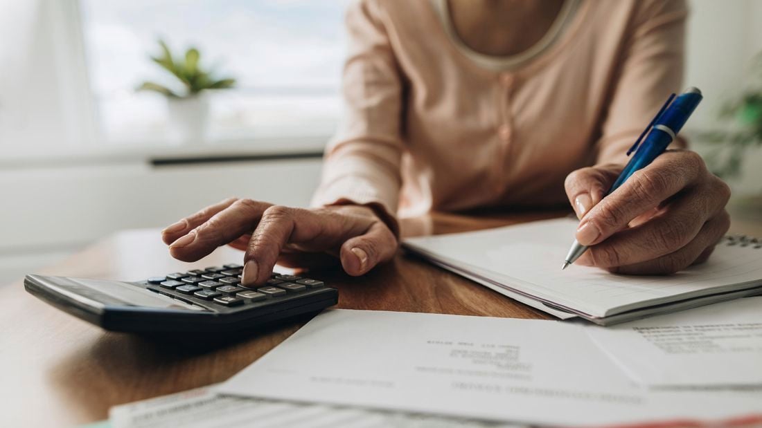 A woman calculating tax using a calculator, paper and pen.