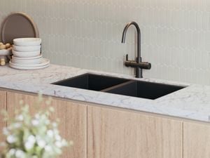 Kitchen sink with a matte black mixer tap set into a white stone benchtop, featuring light hexagon tile splashback and timber cabinetry.