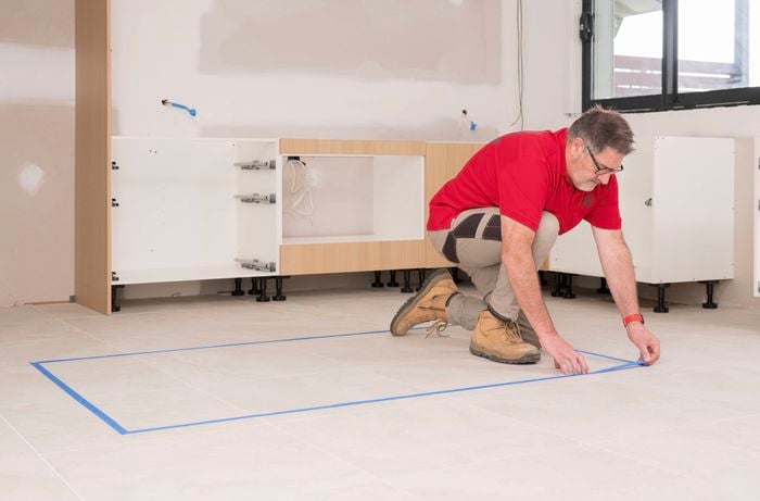 A Bunnings Team Member is applying masking tape on the tiled floor to mark the layout for an island cabinet installation.