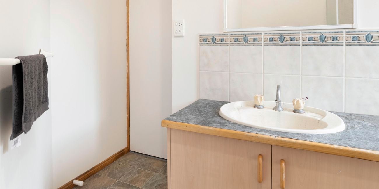 Old bathroom with dated tiles, vanity and flooring.