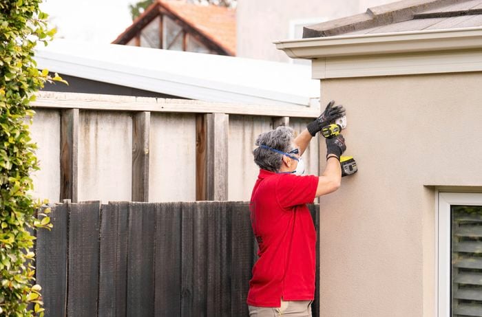 A Bunnings Team Member is using a power drill to attach a mounting bracket onto the wall.