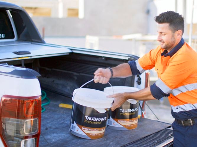 A tradie unloading paint tubs from the back of a ute.