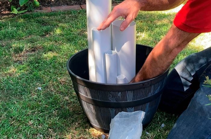 A Bunnings Team Member holding 5 PVC pipes in a pot outside.