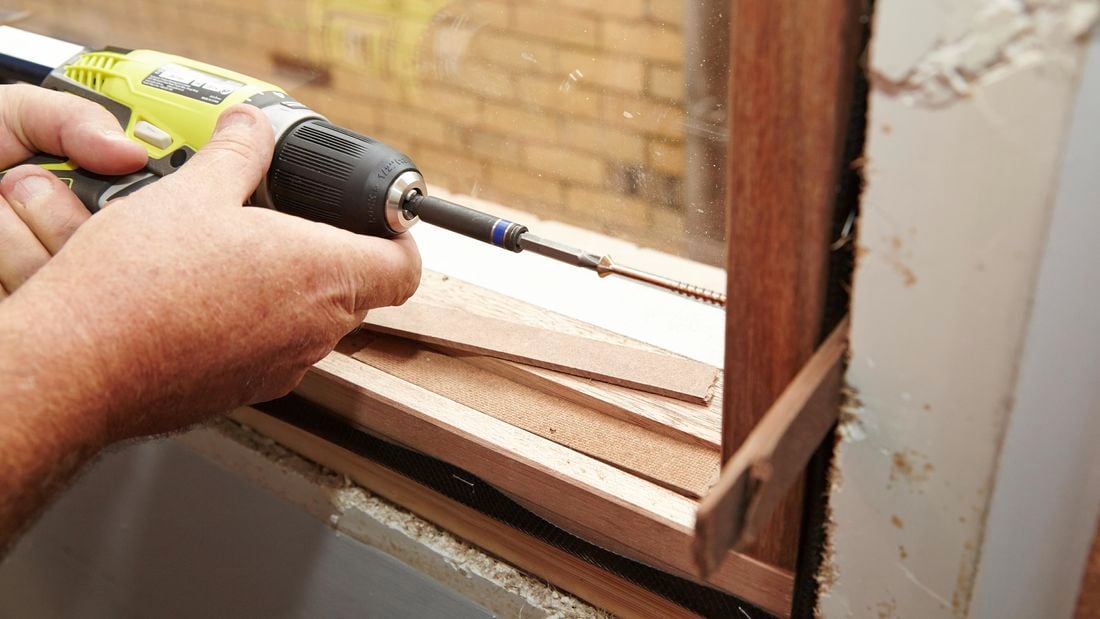 Driving screws through the pilot holes and into the frame of the house