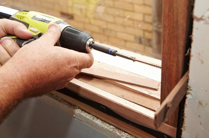 Driving screws through the pilot holes and into the frame of the house