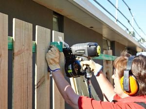 Person attaching fence palings to timber rails using a nail gun
