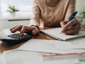 A woman calculating tax using a calculator, paper and pen.