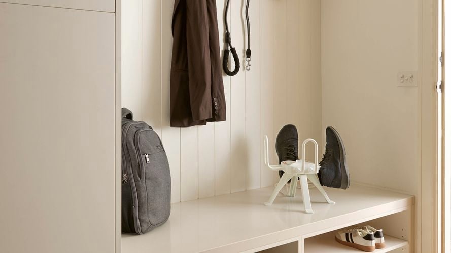 A wall with hooks on it and shelves at the bottom of it with items on them and cupboards next to it.