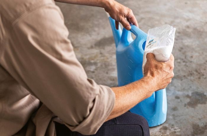 A man in a tan shirt pours Dy-Mark epoxy etching powder into a watering can