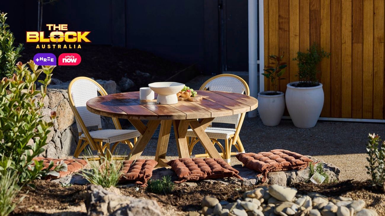 An outside area with a table and chairs, plants, rocks and pot plants in it.
