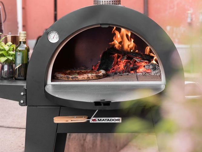 Matador pizza oven with a cooked pizza inside and fire burning.