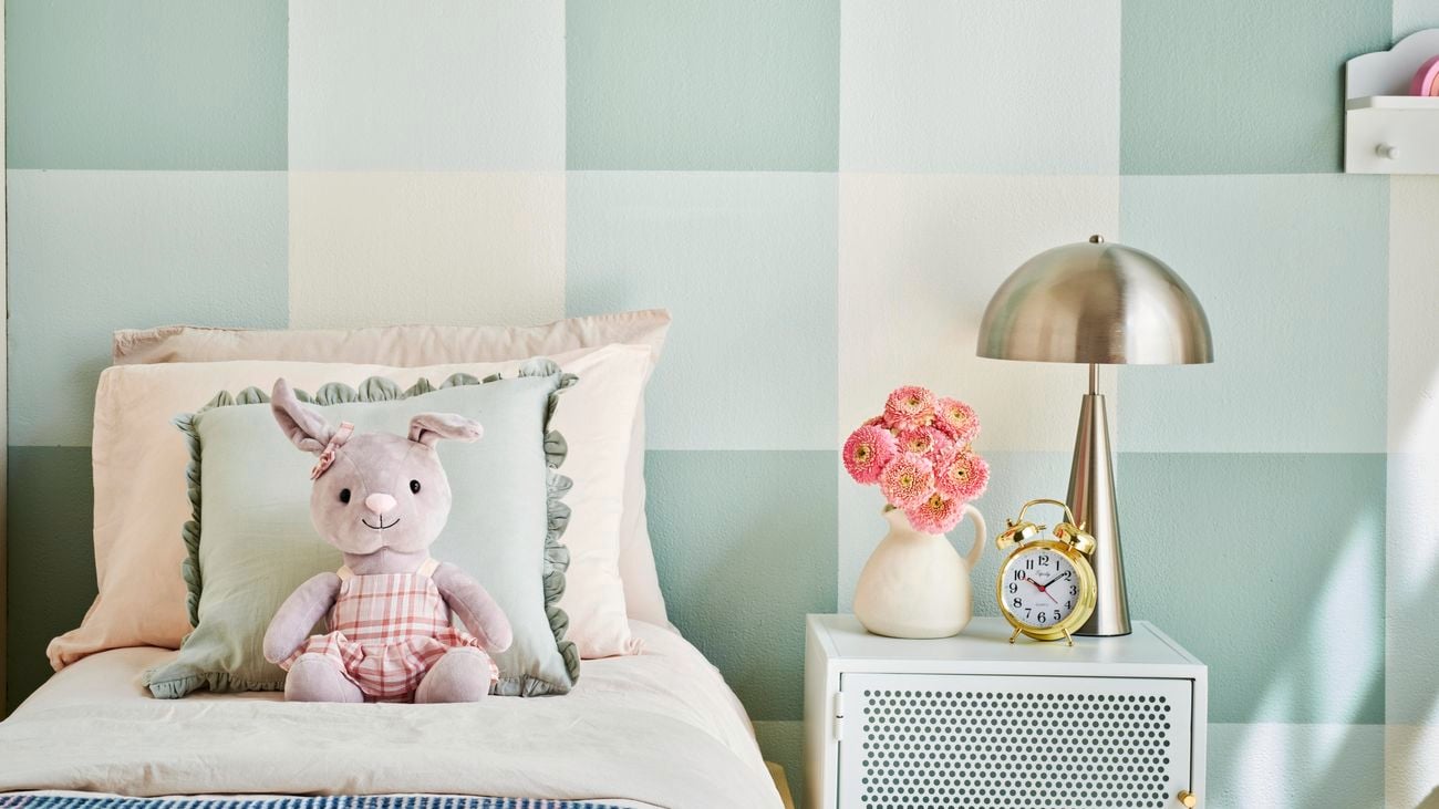 Bed with stuffed toy bunny on top in from of a blue and white gingham feature wall.