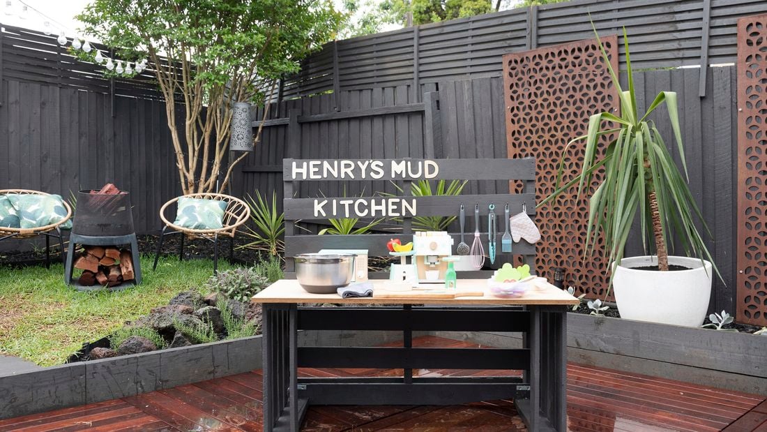 A play kitchen on a deck in a small backyard with Henry's Mud Kitchen signage