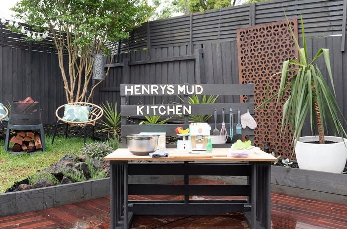 A play kitchen on a deck in a small backyard with Henry's Mud Kitchen signage