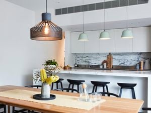 Large pendant light hanging above a dining table with a kitchen in the background and three smaller pendant lights.