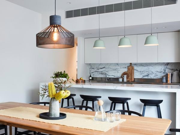 Large pendant light hanging above a dining table with a kitchen in the background and three smaller pendant lights.
