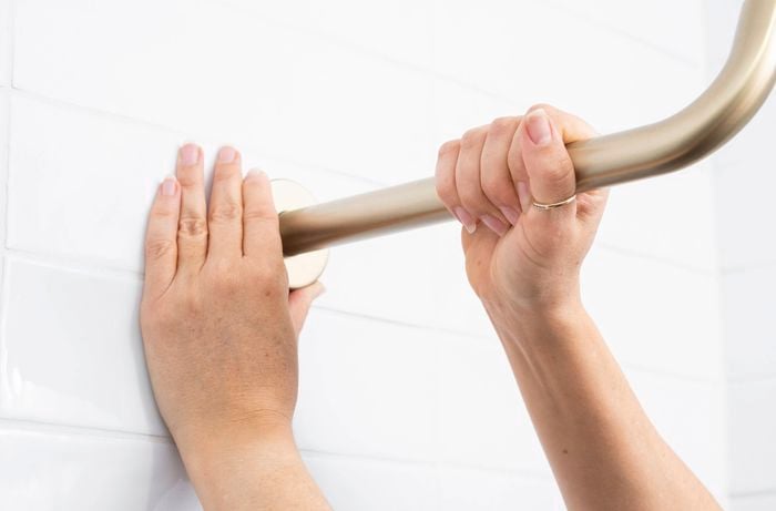 A person is installing a new shower arm onto the existing shower outlet by turning it clockwise. 