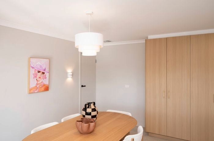 A pendant light hangs over a wooden dining table with vases, complemented by soft wall lighting and a colorful portrait for visual interest. 