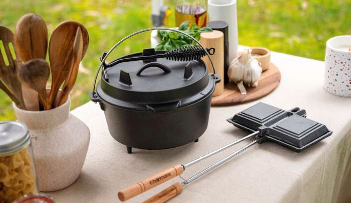 A table outdoors with cooking utensils, ingredients and a cooker.