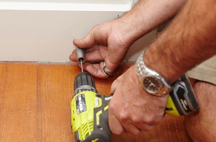 A person drilling through a door stop held against skirting board